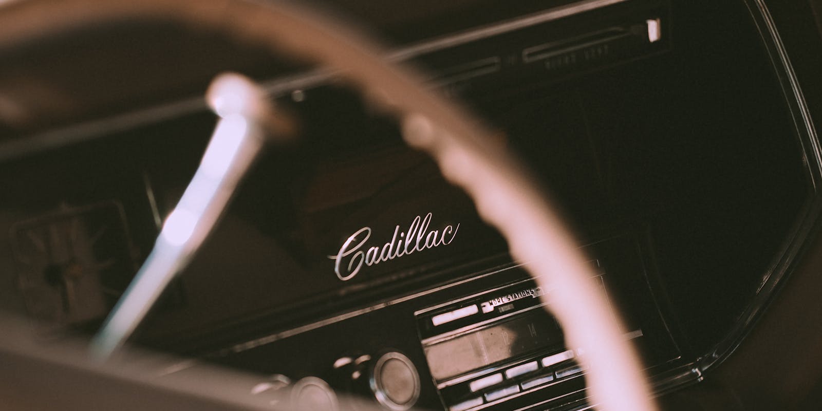 Close-up of a vintage car dashboard featuring the "Cadillac" logo, with a focus on the steering wheel and radio controls.