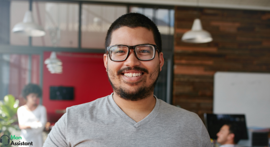 Homme souriant portant des lunettes dans un bureau moderne, faisant partie de l'équipe d'assistance virtuelle de MonAssistant.