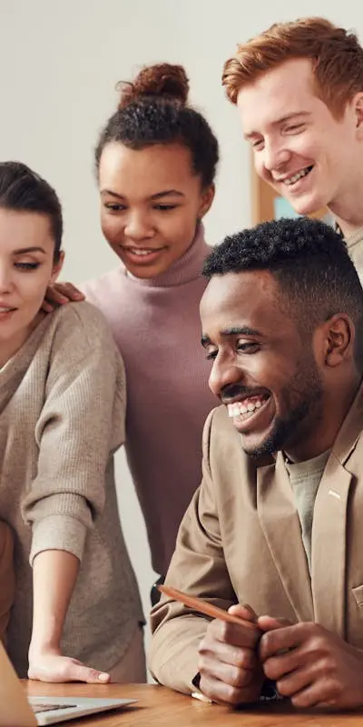 Groupe de jeunes professionnels souriants collaborant autour d'un ordinateur portable, représentant un environnement de travail d'équipe dynamique et positif.