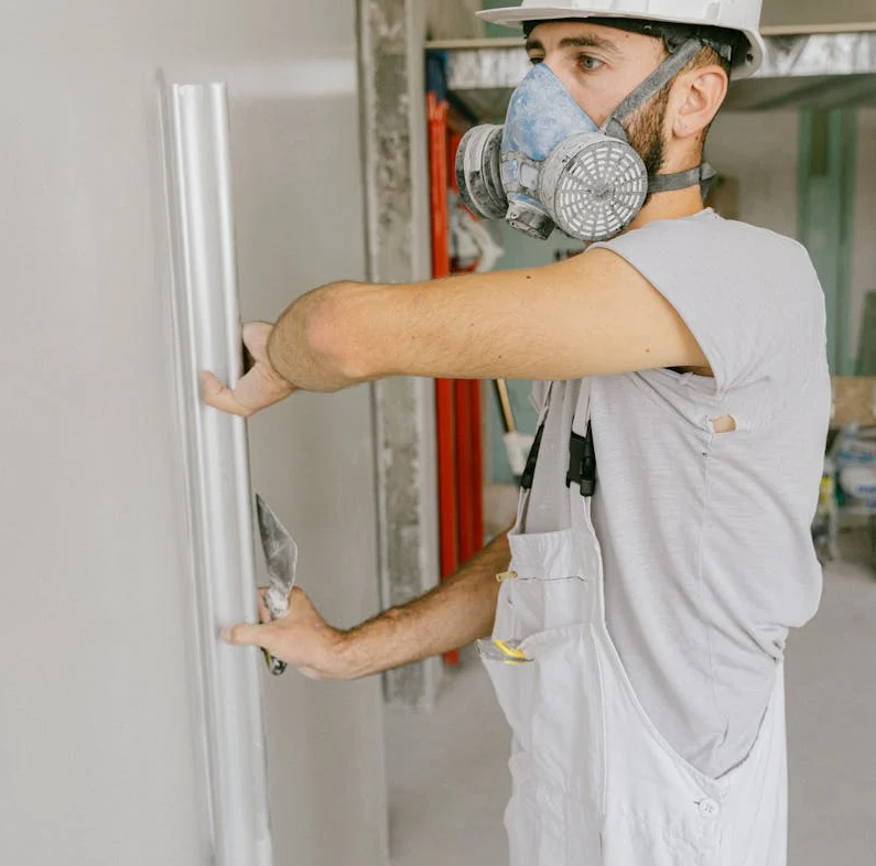 A man in a gas mask stands holding a door, suggesting a scene of urgency or protection in a hazardous environment.