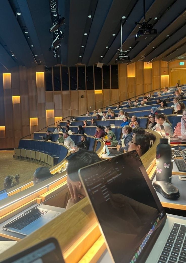 Amphithéâtre rempli d'étudiants avec des ordinateurs portables ouverts, lors d'un cours ou d'une conférence