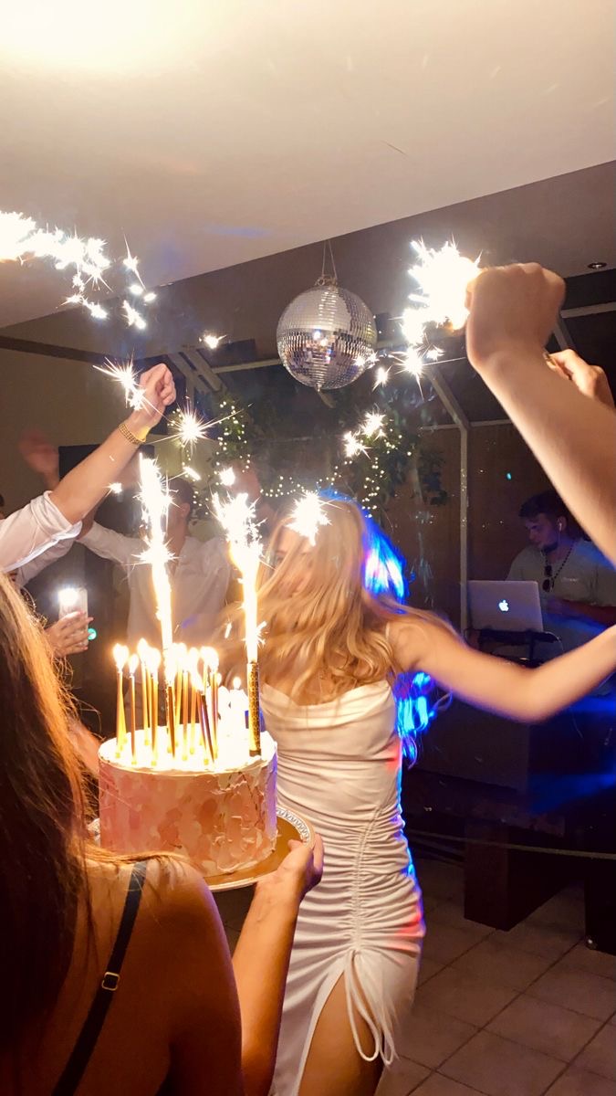 Fête d'anniversaire avec une femme en robe blanche, un gâteau illuminé de bougies et des étincelles festives