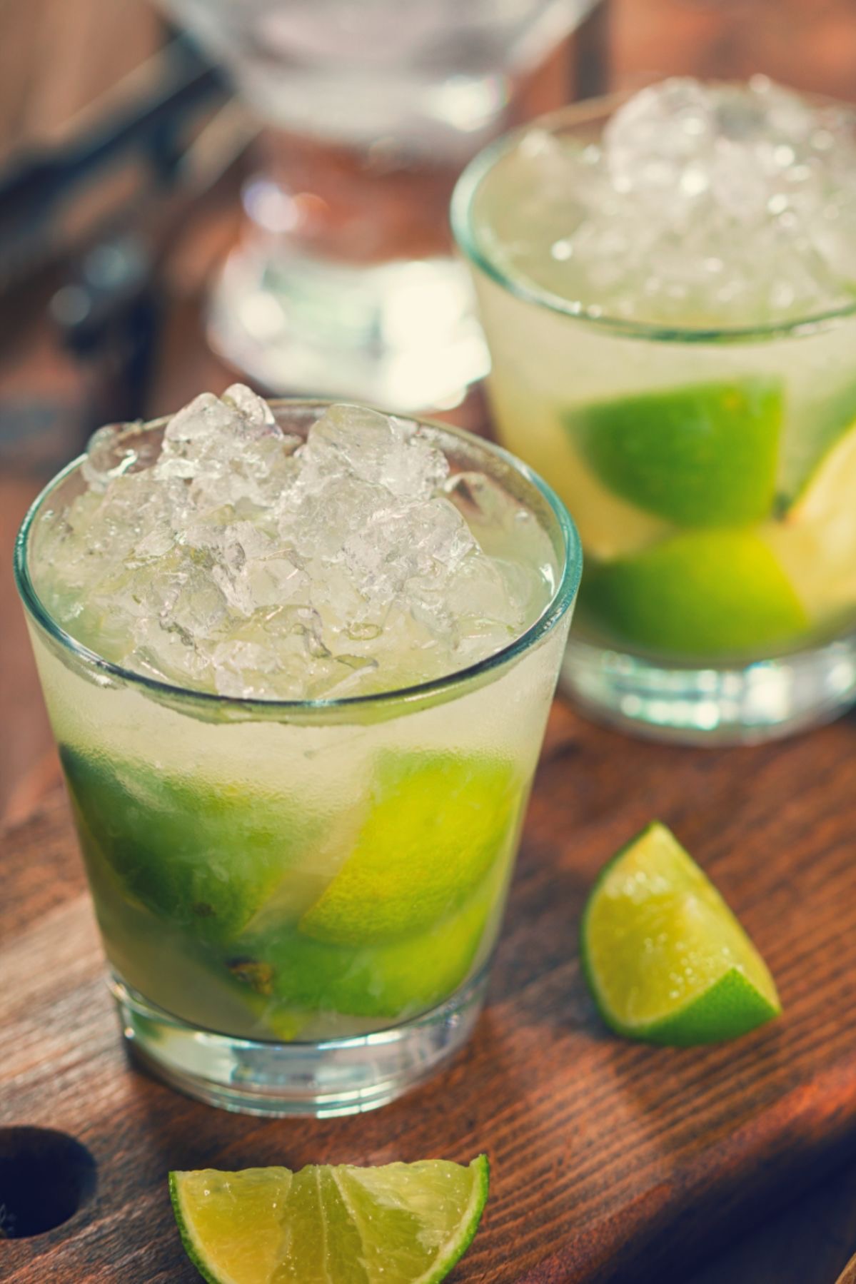 Deux verres de Ti Punch, garnis de quartiers de citron vert et de glace pilée, posés sur une table en bois