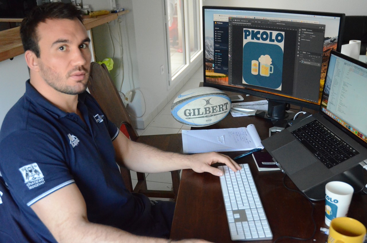 Un homme assis à un bureau, travaillant sur la conception graphique de l'application Picolo affichée à l'écran, avec un ballon de rugby Gilbert en arrière-plan.
