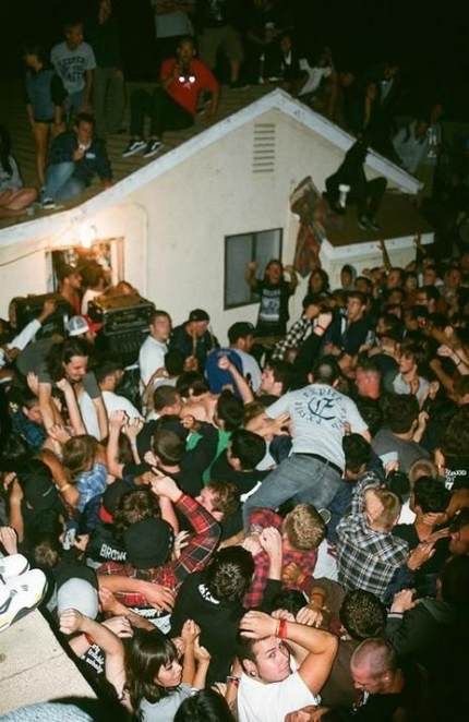 Foule dense lors d'une fête en extérieur, des personnes debout sur un toit et d'autres en train de danser ou de se bousculer