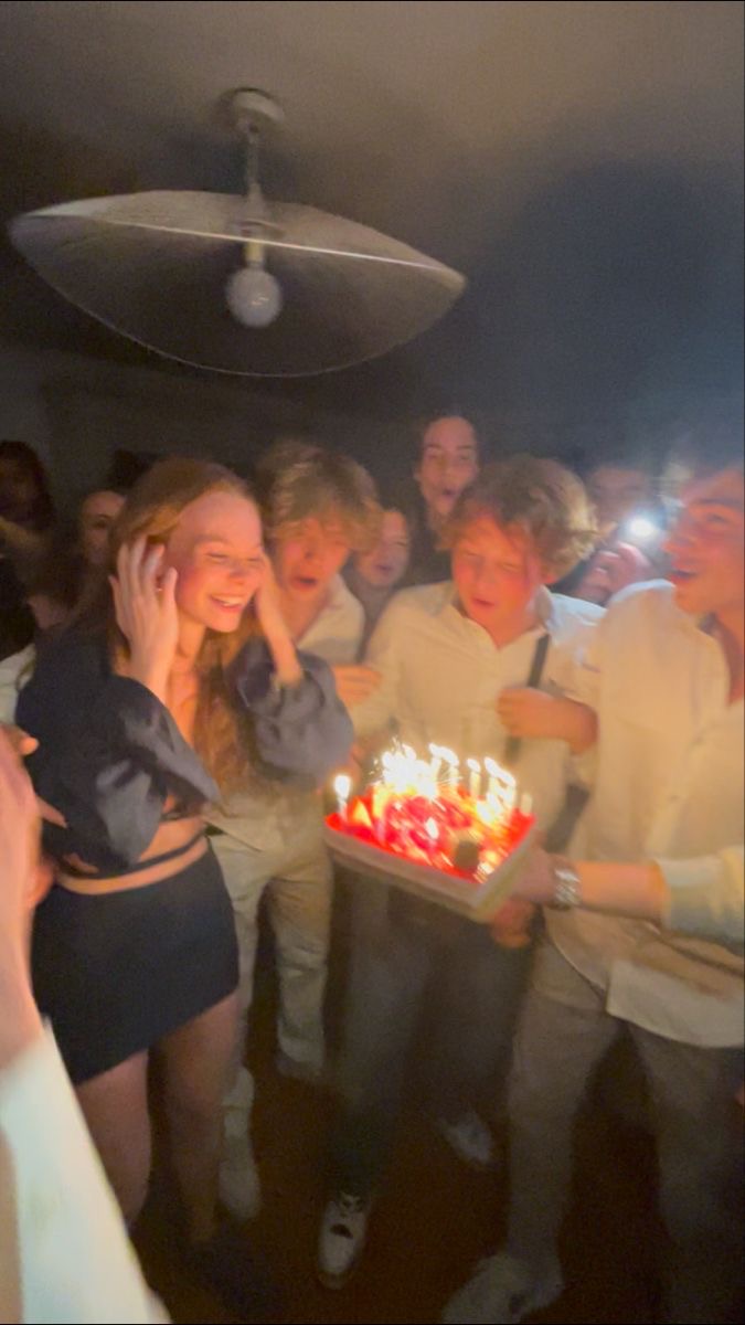 Scène d'anniversaire avec une jeune femme entourée d'amis et un gâteau illuminé de bougies