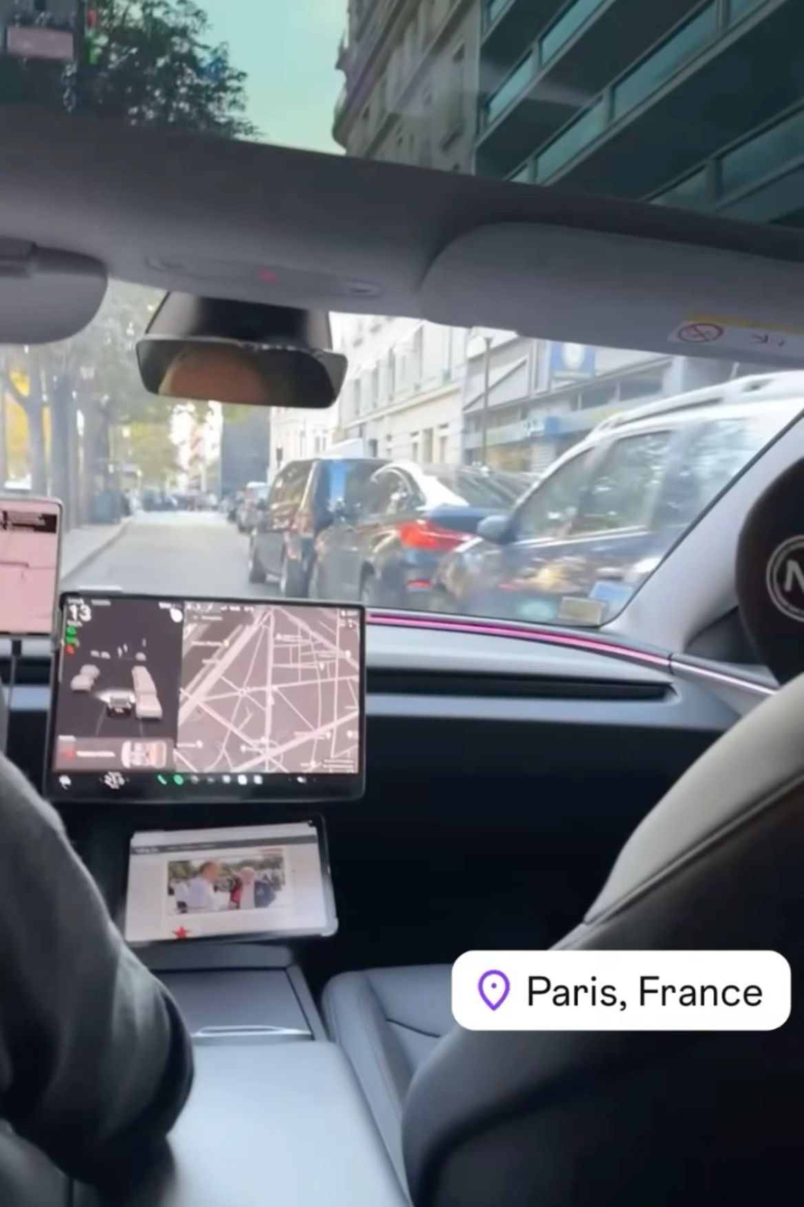 Vue depuis l'intérieur d'une voiture avec un écran de navigation affichant une carte, dans une rue de Paris