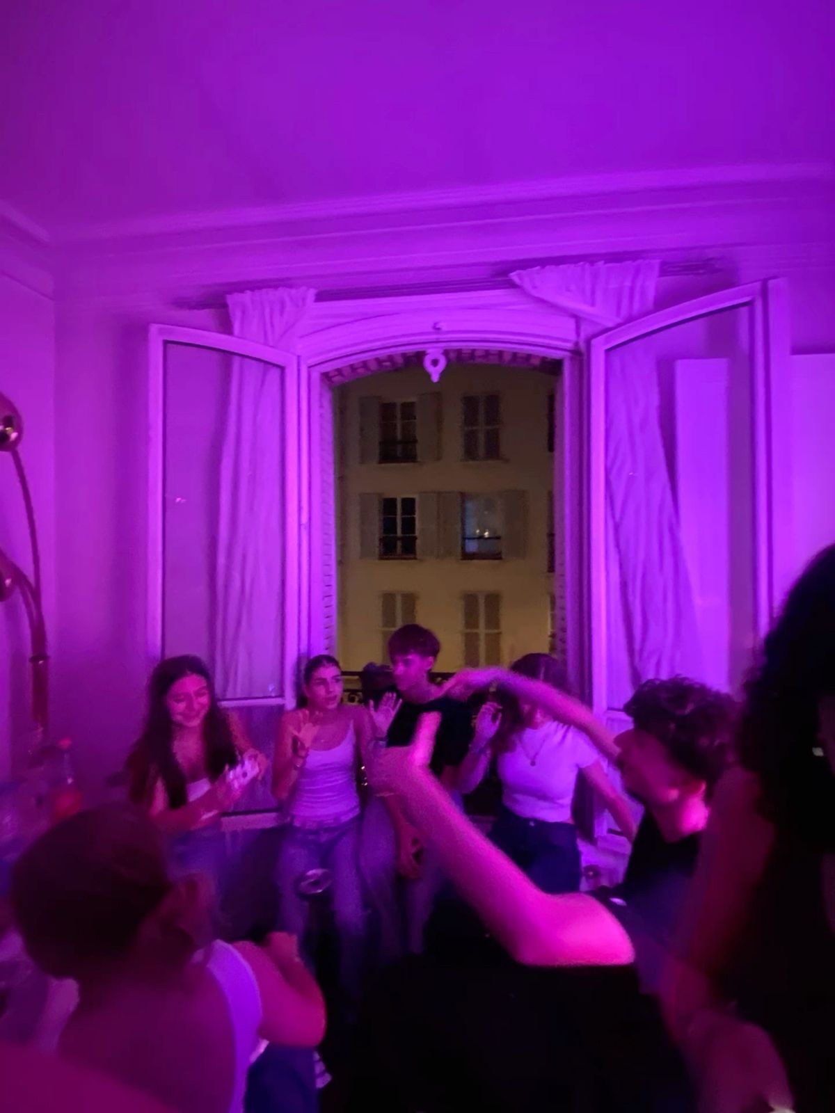Groupe de personnes réunies dans une pièce à l'éclairage violet, profitant d'une ambiance détendue près d'une fenêtre ouverte