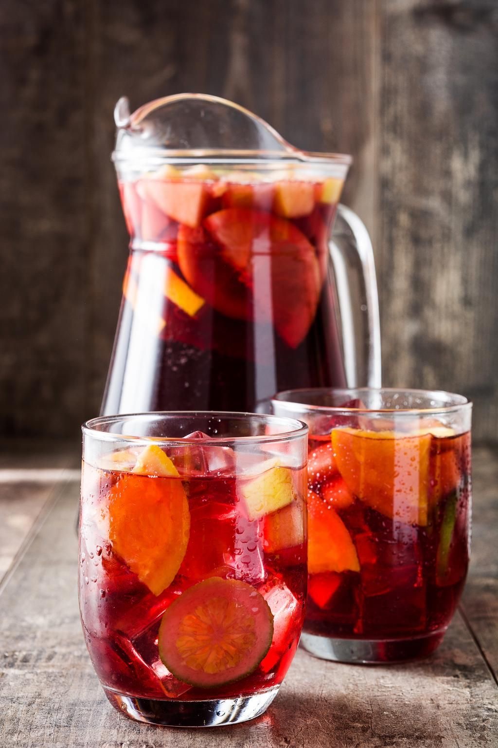 Carafe et verres de sangria rouge garnis de tranches d'orange, de citron et de fruits frais, posés sur une table en bois rustique
