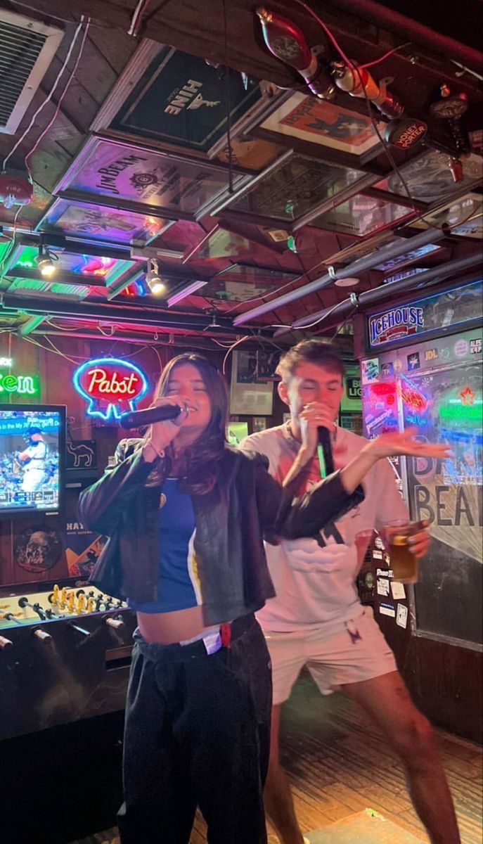 Deux personnes chantant au karaoké dans un bar coloré et animé, avec une ambiance festive