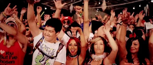 Foule festive en costumes, avec des personnes dansant et levant les bras lors d'un événement animé